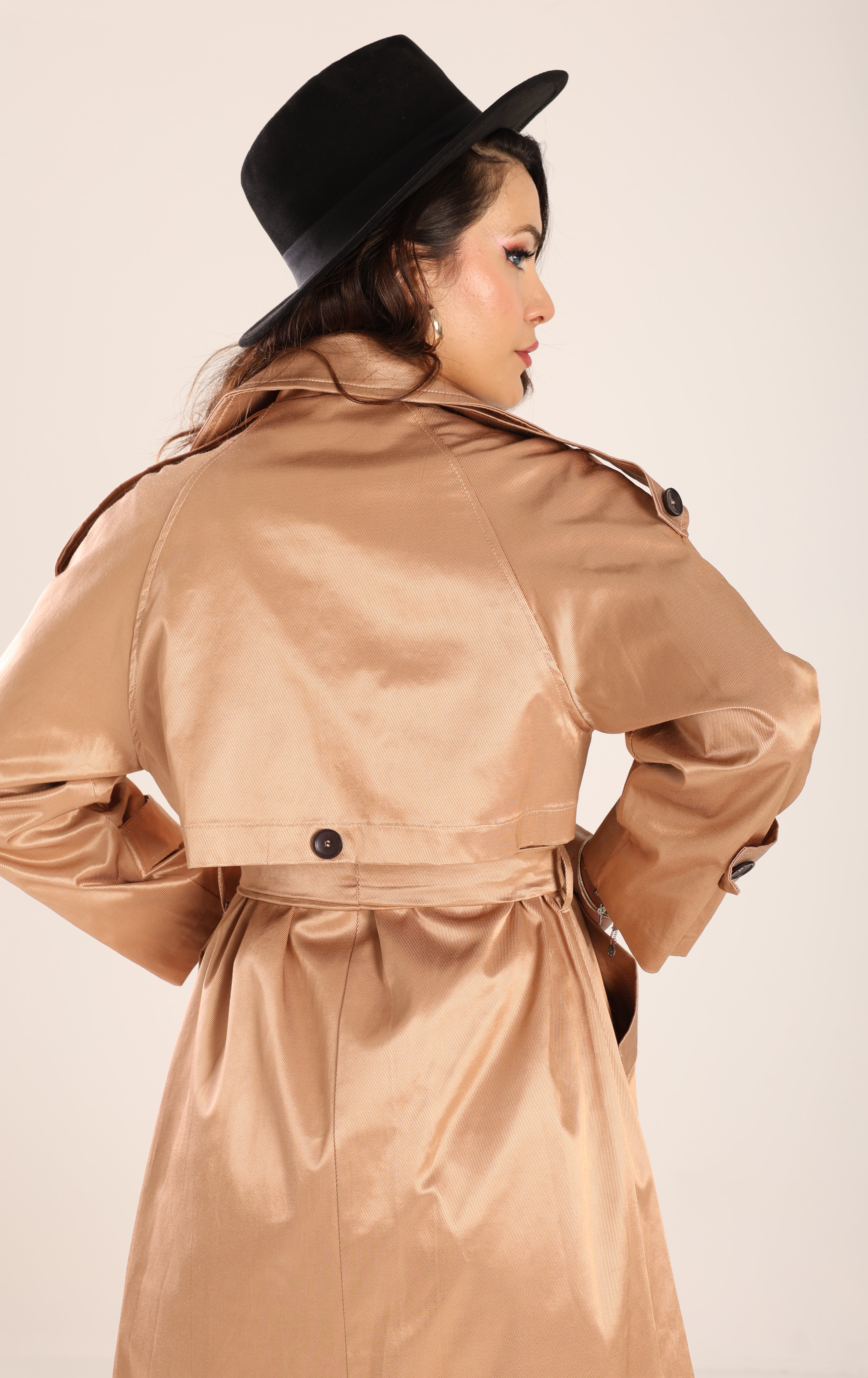 Woman wearing a beige trench coat and black hat against a plain background