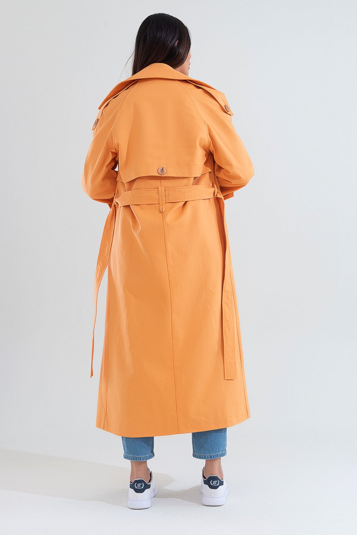 Person wearing an orange trench coat on a white background