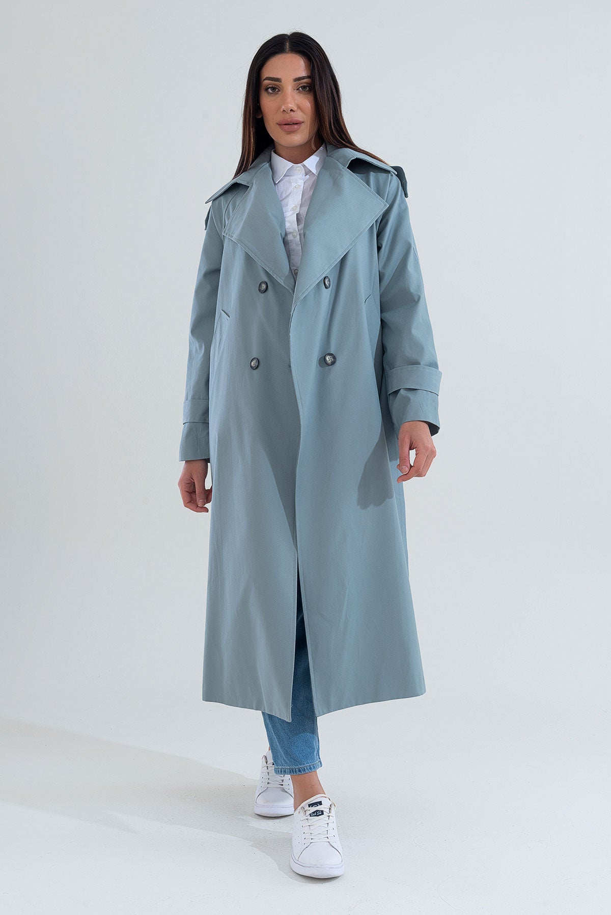 Woman wearing a long light blue trench coat on a white background