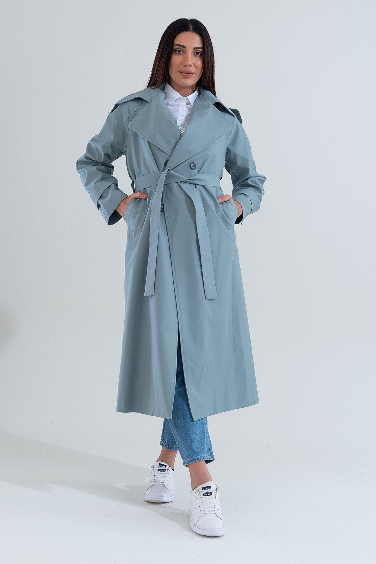 Woman wearing a light blue trench coat on a white background