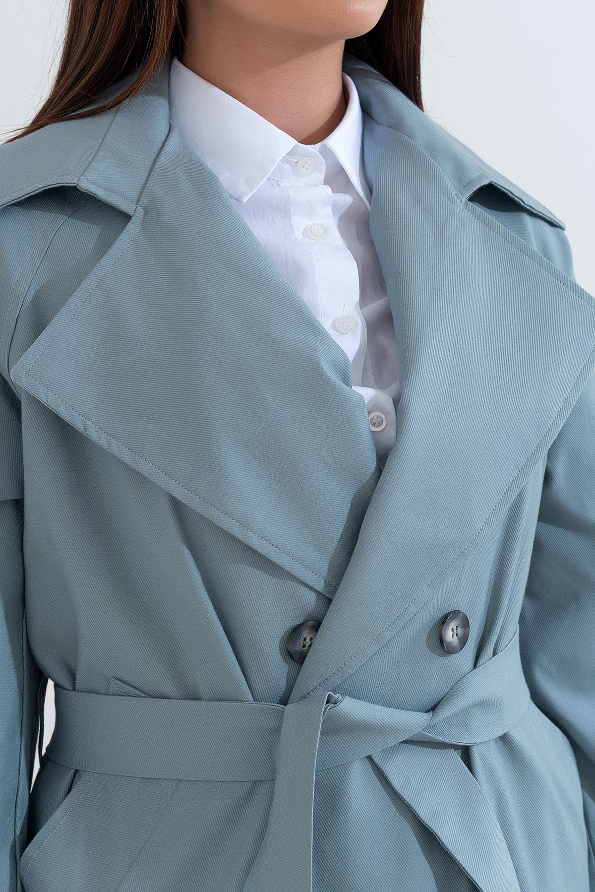 Light blue trench coat worn by a person with a white shirt underneath, on a plain background