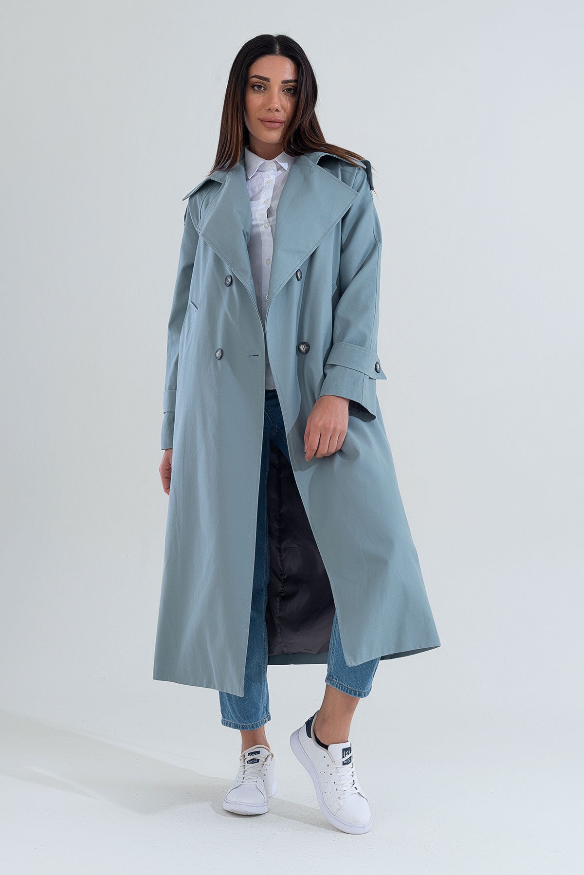 Woman wearing a long light blue trench coat on a white background