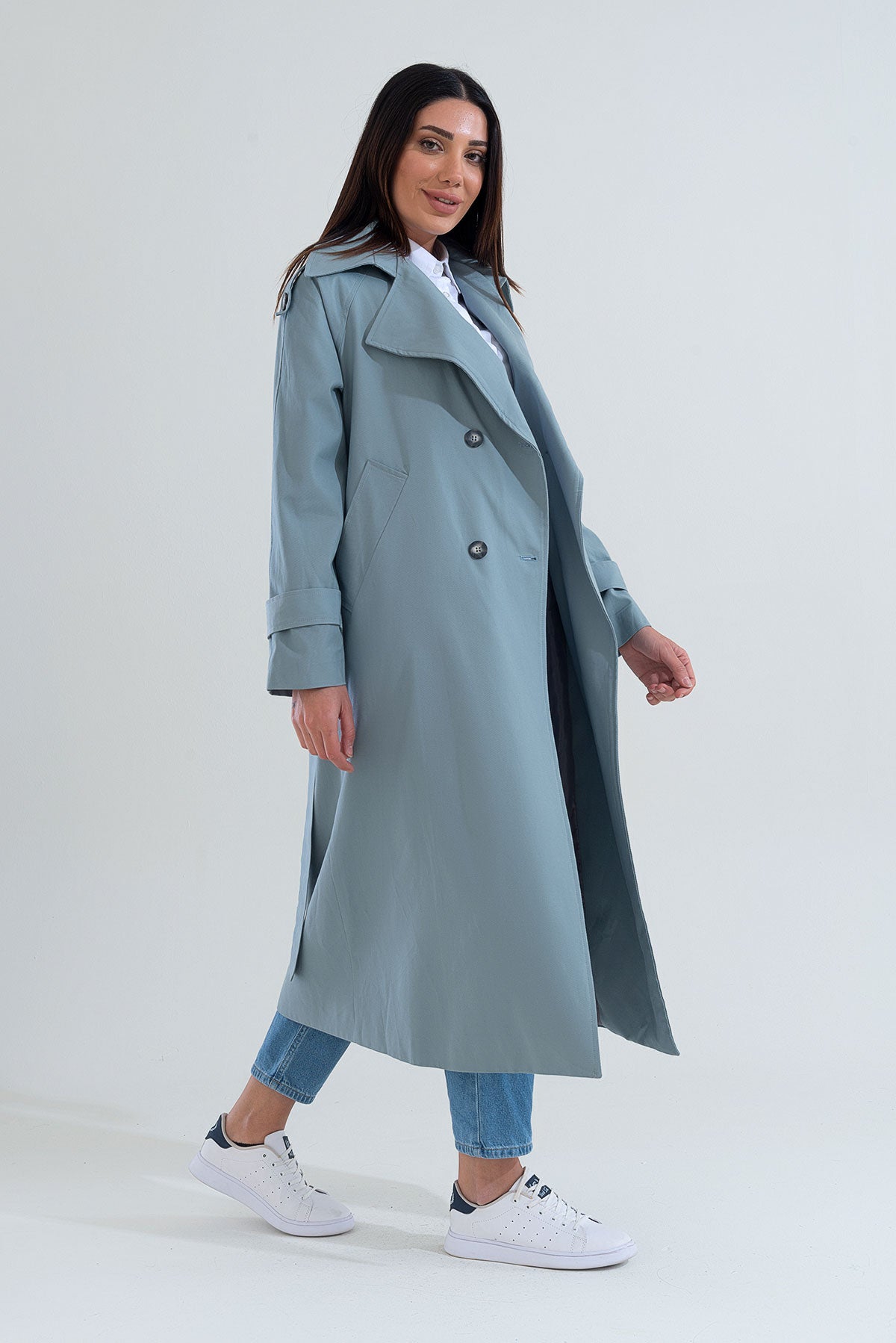 Woman wearing a long light blue coat on a white background