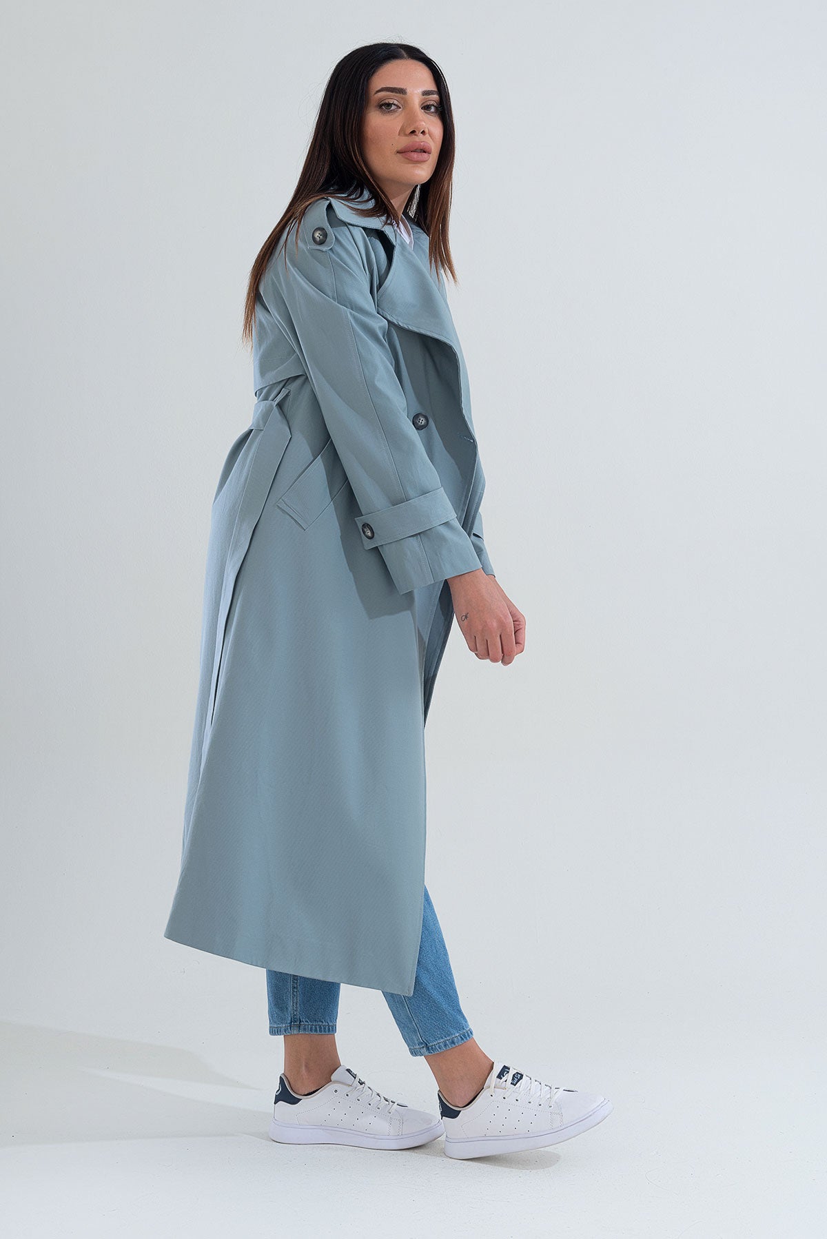 Woman wearing a light blue trench coat on a white background