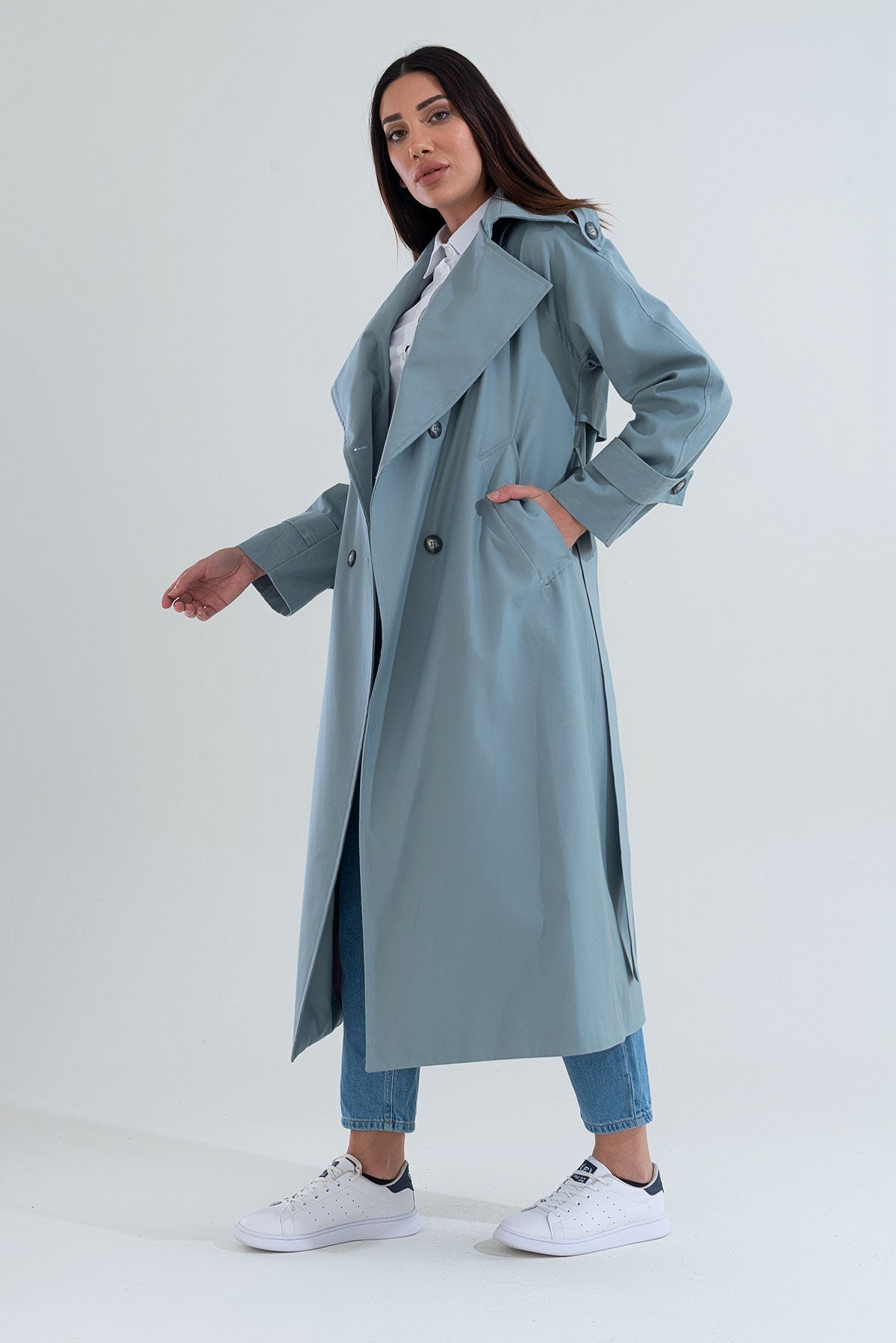 Woman wearing a long light blue coat on a white background