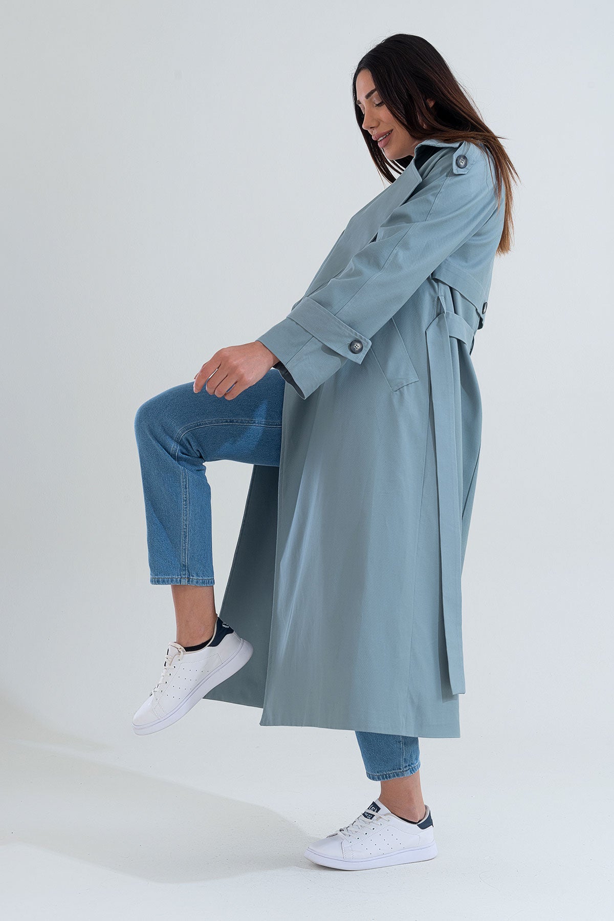 Woman wearing a light blue trench coat and jeans on a white background