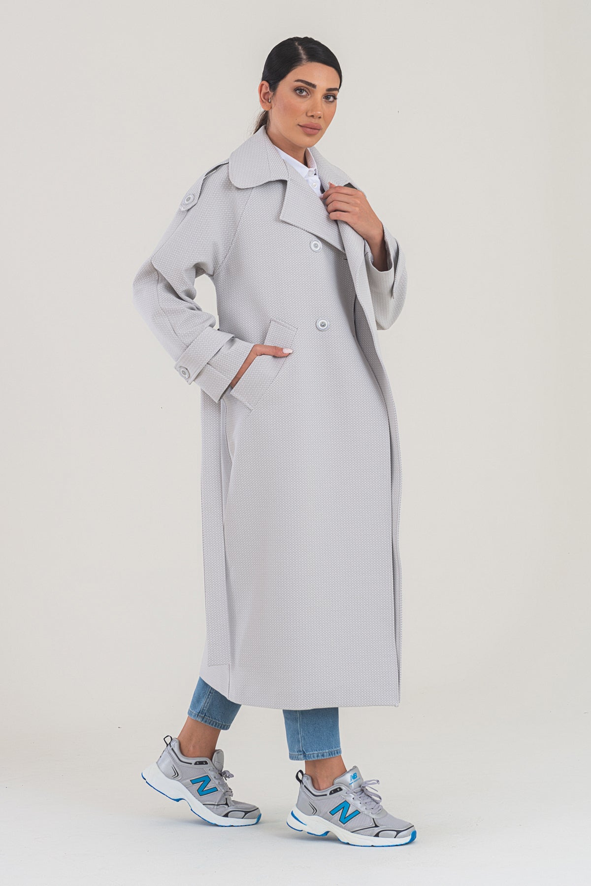 Woman wearing a long light gray coat on a white background
