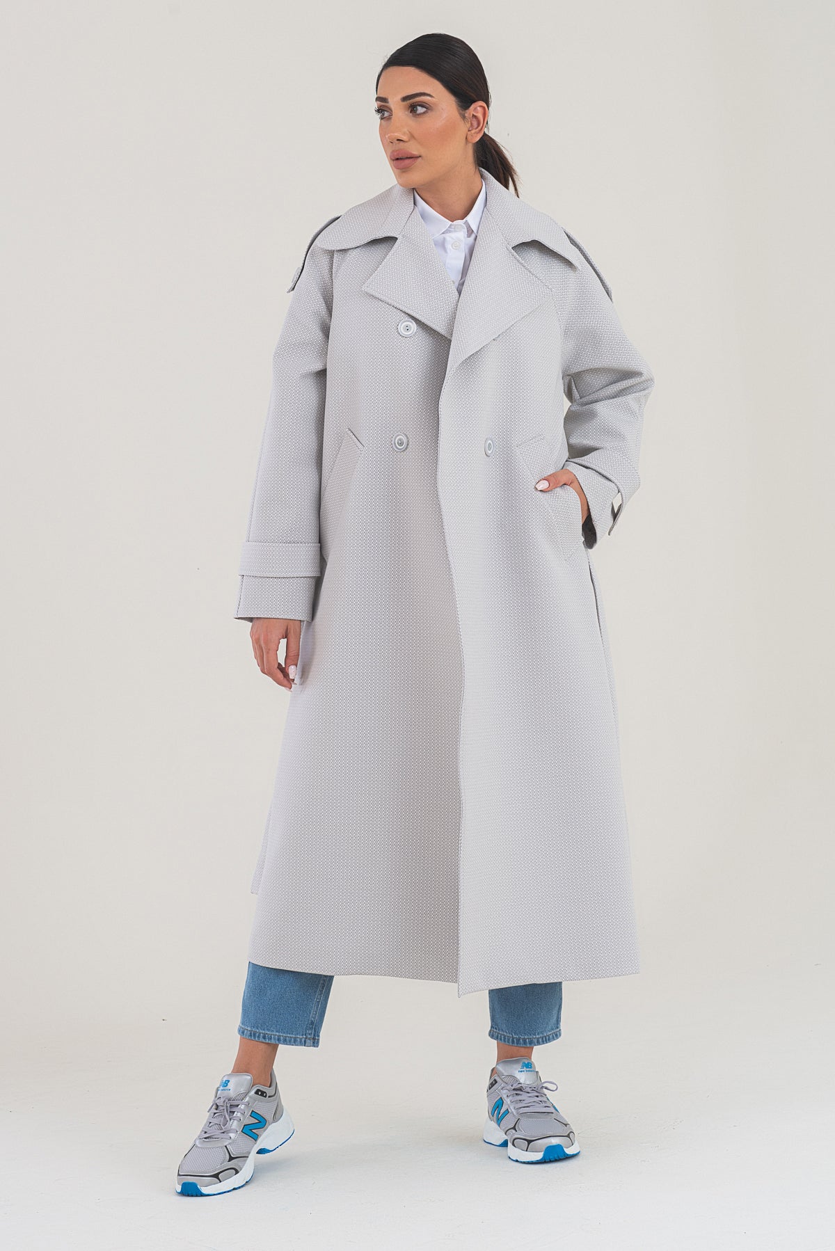 Woman wearing a long light gray coat on a white background
