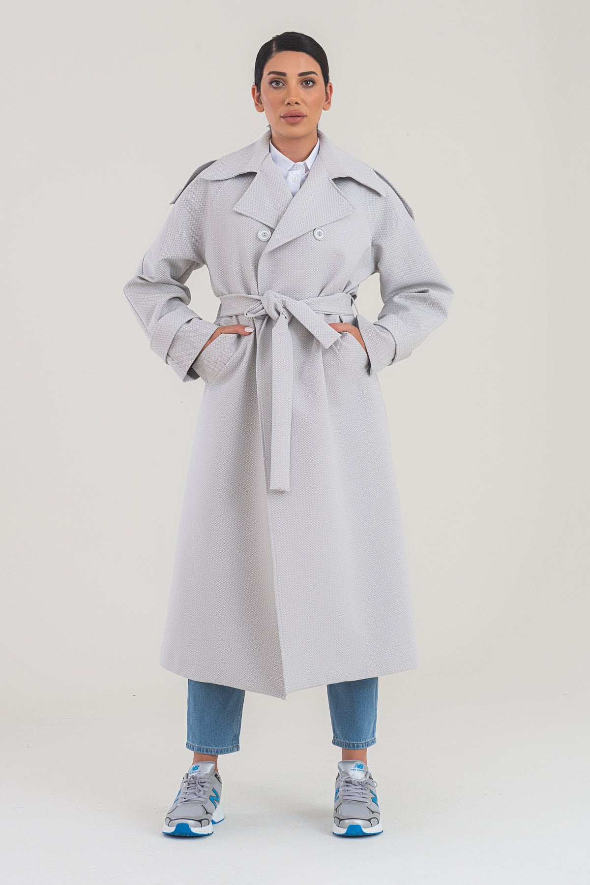 Person wearing a light gray trench coat on a white background