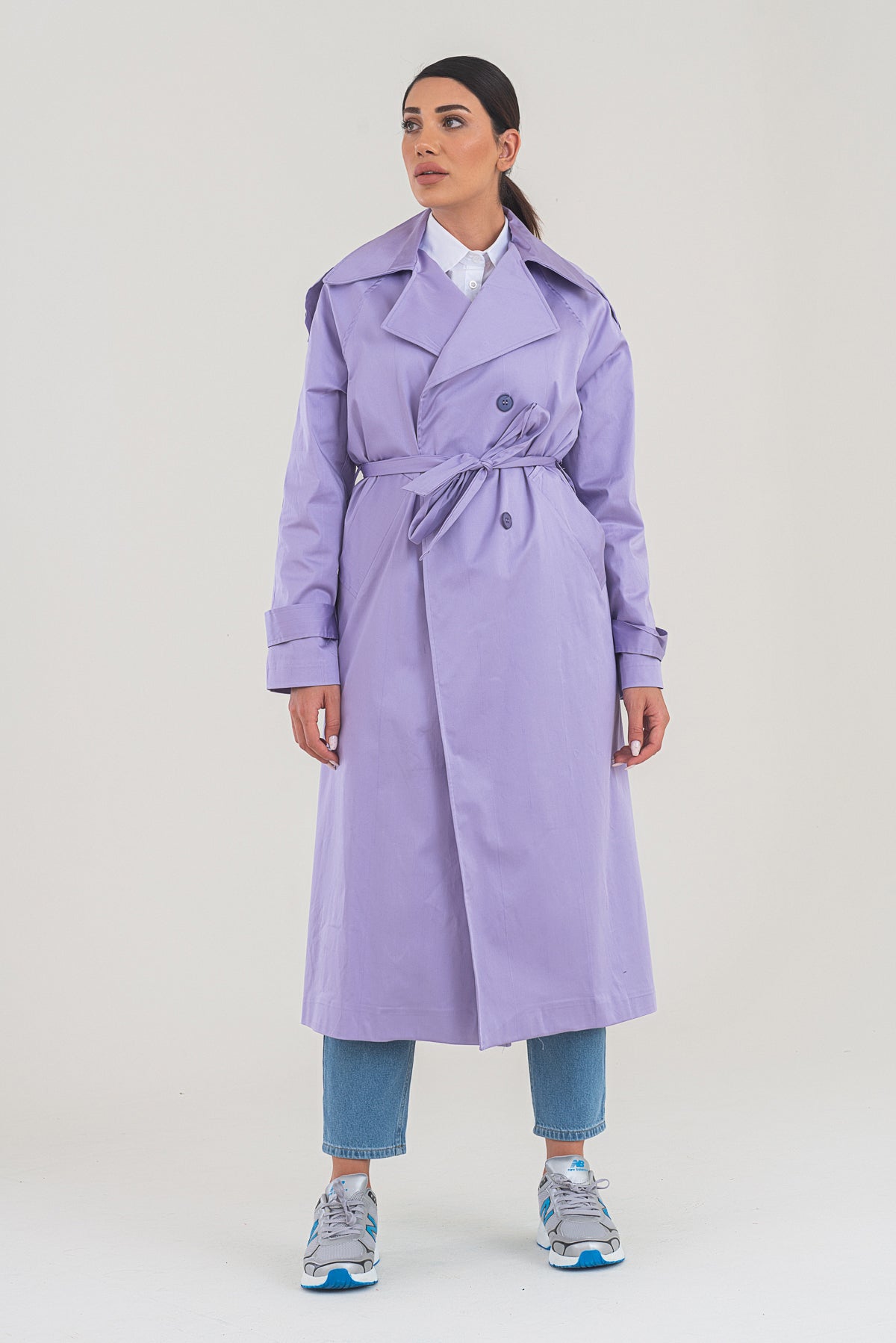 Woman wearing a long lavender trench coat on a white background