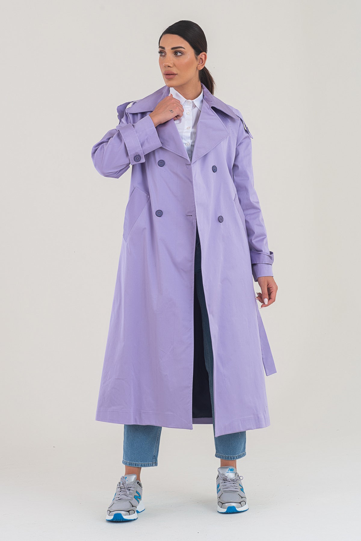 Woman wearing a long lavender coat on a plain background
